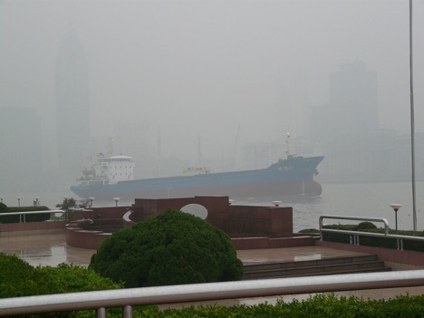 Smog in Shanghai makes the skyscrapers barely visible as a large ship moves on the river.