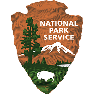 Logo for the National Park Service, shaped like an arrowhead and containing a green-and-orange scene with a buffalo, a forest, and a snow-capped mountain.