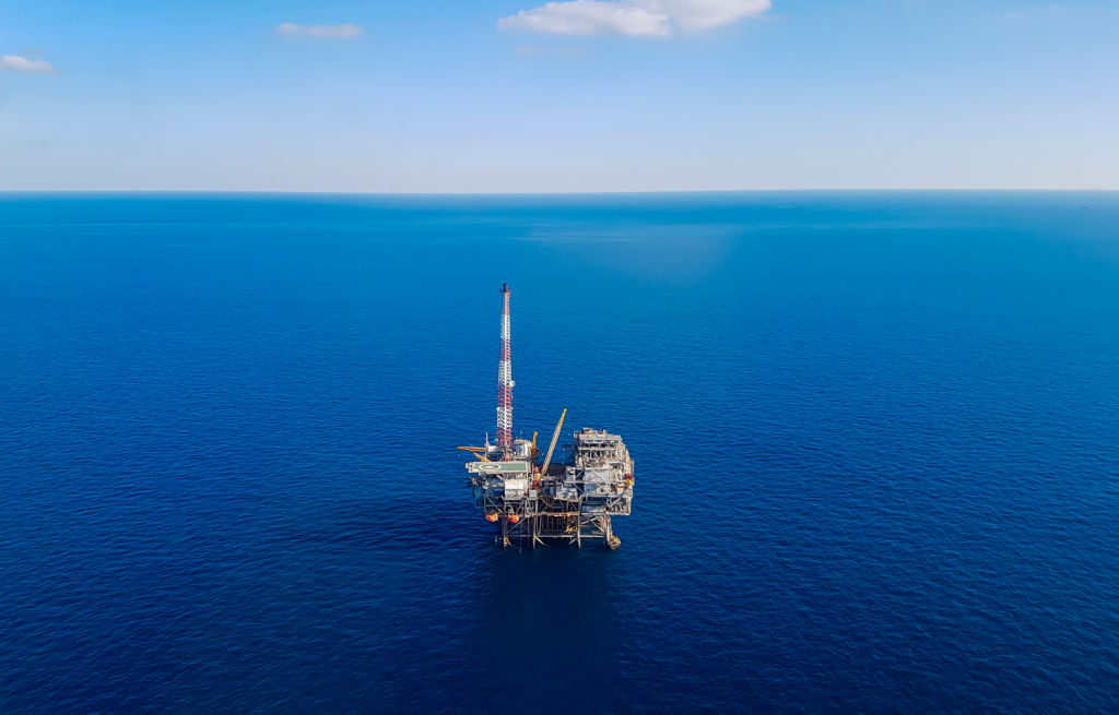 An oil rig out in the middle of a blue ocean on a sunny day.